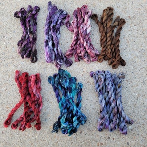 以下が含まれることがあります： 紫、ピンク、青、ターコイズ、茶色など、さまざまな色の刺繍糸10巻の詰め合わせ。糸は2巻または3巻のグループにまとめられています。