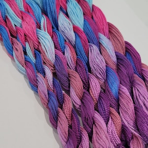 May include: Close-up of braided embroidery floss in a range of pinks, purples, and blues. The threads are arranged diagonally, with a gradient effect from light to dark. The image highlights the texture and colour variations of the threads.