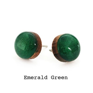 May include: A pair of emerald green stud earrings with a wood base.