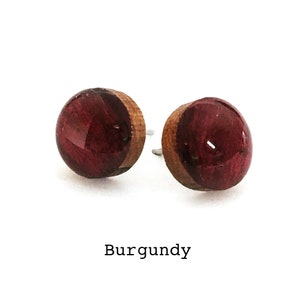 May include: A pair of burgundy wood and resin stud earrings. The earrings are round and have a wood backing.