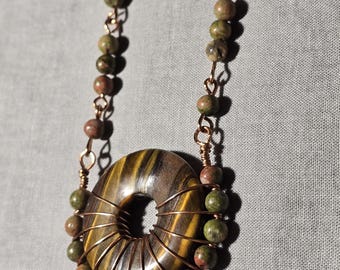 May include: A copper wire wrapped tiger's eye stone donut pendant necklace with green and brown jasper beads.