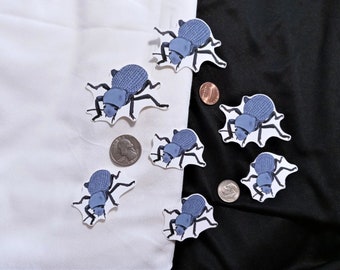 May include: Eight blue beetle stickers on a white and black background. The stickers are of a cartoon beetle with a spiky shell and six legs.