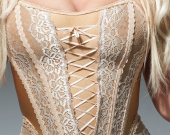 May include: A beige lace corset with a satin ribbon lacing up the front. The corset has a delicate floral pattern and a scalloped hem.