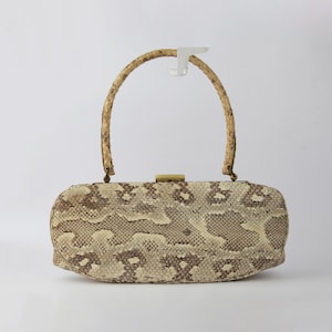 Op de afbeelding: Een rechthoekige handtas met een slangenpatroon in beige en bruine tinten. Hij heeft een gebogen handvat en een goudkleurige sluiting. De tas staat tegen een effen witte achtergrond.