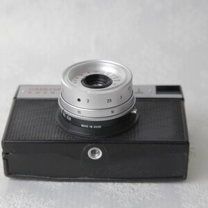 May include: A black and silver 35mm film camera with a lens that has a depth of field scale marked in numbers from 2 to 250. The camera is made in the USSR.