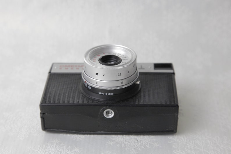 May include: A black and silver 35mm film camera with a lens that has a depth of field scale marked in numbers from 2 to 250. The camera is made in the USSR.