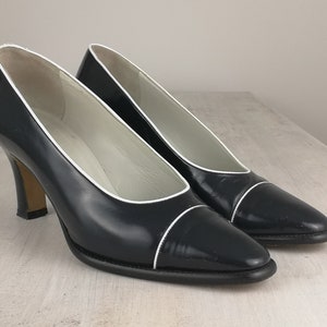May include: A pair of black leather pumps with white trim around the toe and heel. The shoes have a pointed toe and a high heel.