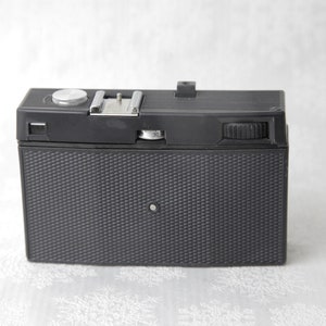May include: A black vintage film camera with a silver knob and a textured black body.