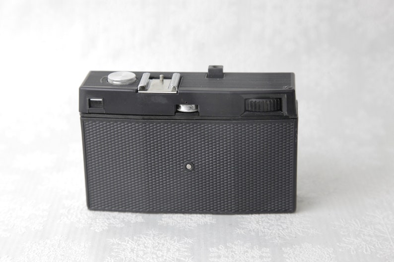 May include: A black vintage film camera with a silver knob and a textured black body.