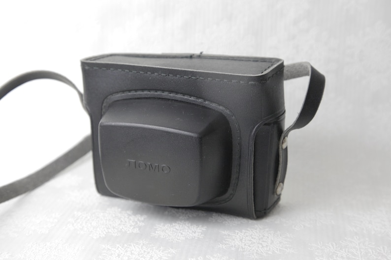 May include: Black leather camera case with a strap and the word "LOMO" embossed on the front.
