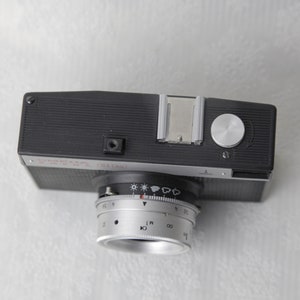 May include: A black and silver Seagull camera with a lens that has a dial for adjusting the aperture and shutter speed. The camera has a built-in flash and a hot shoe.
