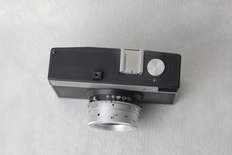 May include: A black and silver Seagull camera with a lens that has a dial for adjusting the aperture and shutter speed. The camera has a built-in flash and a hot shoe.