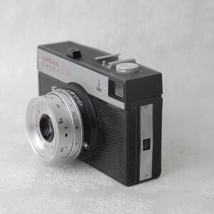 May include: A black and silver 35mm film camera with a silver lens and a black textured body. The camera has a silver nameplate that reads "Corona" and "Corona 35S".