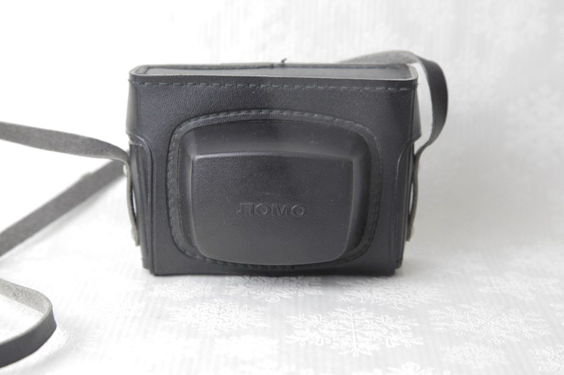 May include: Black leather camera case with a strap and the word "TOMO" embossed on the front.