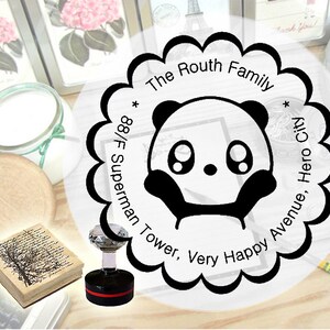 K&ouml;nnte beinhalten: Eine Schwarzwei&szlig;-Illustration eines Pandas mit gro&szlig;en Augen und einer kleinen Nase. Die Illustration ist von einem Kreis mit dem Text "The Routh Family * 88/F Superman Tower, Very Happy Avenue, Hero City *" in Schwarz umgeben.
