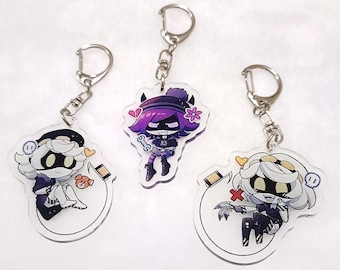 May include: Three acrylic keychains featuring anime-style characters. Each keychain has a silver-colored metal ring and clasp. The characters have black and white outfits with colorful hair and accessories. One character holds a bone, another has a heart.