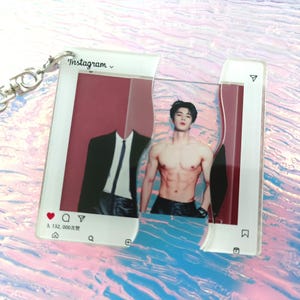 May include: A clear acrylic keychain featuring a split Instagram-style interface design. The left side shows a suit jacket and tie, while the right side displays a shirtless person with dark hair. The frame includes icons and the text Instagram.