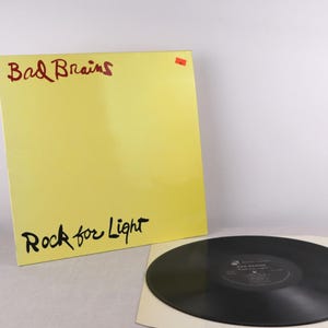 May include: A white ceramic mug with a black handle and the text "But First, Coffee" in a black, bold font. The mug is on a white surface. The mug is approximately 4 inches tall.