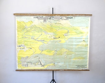 May include: Vintage map print with Greek text, featuring a detailed landscape in shades of yellow, green, and blue. The map is mounted on wooden dowels and suspended by a string, showcasing a historical geographical illustration.