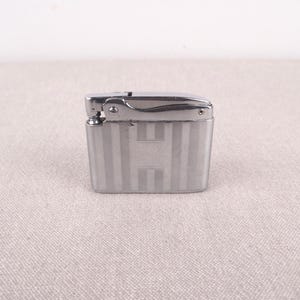 以下が含まれることがあります： ストライプ模様の銀色のライター。ライターは、フリップトップの蓋が付いています。