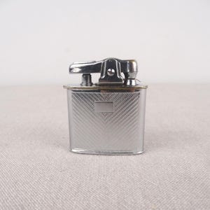 May include: A silver lighter with a textured design and a hinged lid.