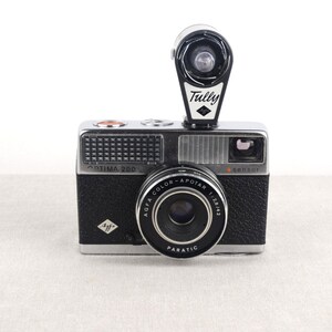 May include: A black and silver Agfa Optima 200 camera with a built-in flash. The camera has a black lens with the text "Agfa Color-Apotar 1:2.8/43 Paratic" printed on it. The flash is a black and white Tully flash with a diamond logo.