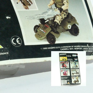 May include: A green and gray toy military vehicle with a large gun, a driver figure, and a star on the side. The vehicle is labeled "G.I. JOE" and "MOTORISED".