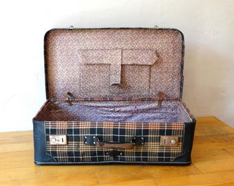 May include: An open vintage suitcase with a black and brown plaid pattern. The inside of the suitcase is lined with a floral pattern.