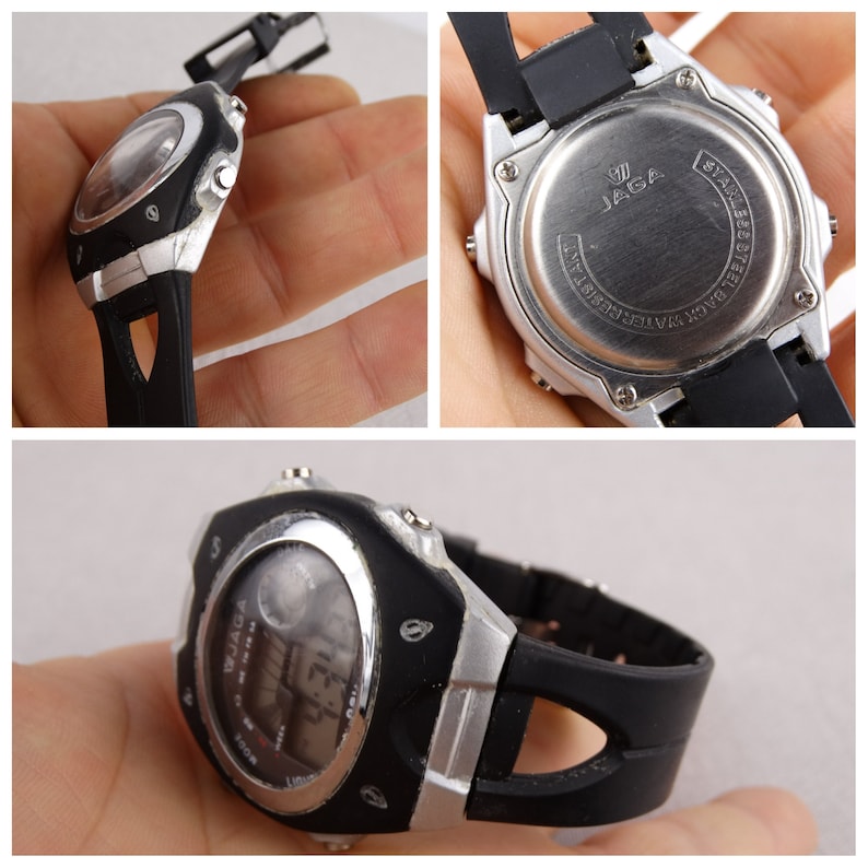 May include: A black and silver digital wristwatch with a black rubber band. The watch face has a silver bezel and a black background with white digital numbers. The watch has a JAGA logo on the back.