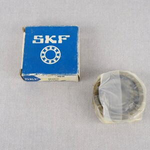 May include: A blue box with the word "SKF" printed on it. The box contains a new SKF bearing. The bearing is in a clear plastic bag.