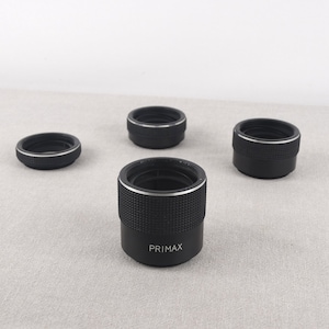 May include: Four black camera lens adapters with silver rings. The adapter in the centre has the word "PRIMAX" printed on it.