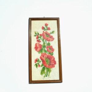 May include: A framed embroidery depicting a bunch of red poppies with green leaves and stems, set against a white background.