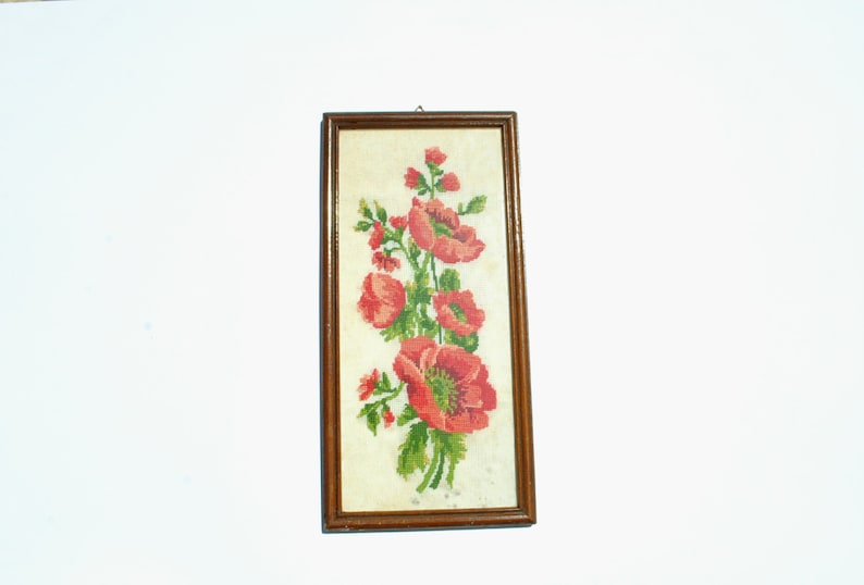 May include: A framed embroidery depicting a bunch of red poppies with green leaves and stems, set against a white background.