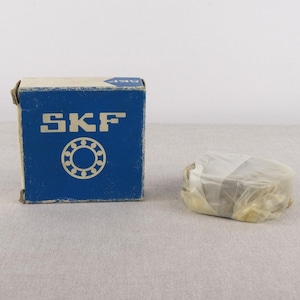 May include: A blue box with the word "SKF" printed on it. The box contains a wrapped ball bearing.