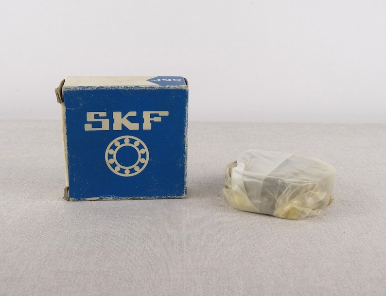 May include: A blue box with the word "SKF" printed on it. The box contains a wrapped ball bearing.