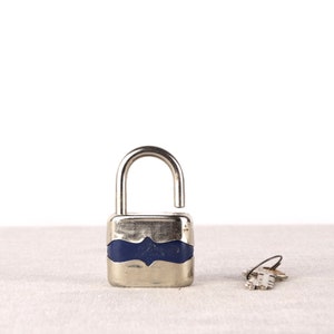 May include: A silver padlock with a blue band around the middle, and a silver key on a white surface.