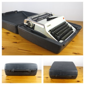 Puede incluir: Una m&aacute;quina de escribir Olympia blanca con teclas negras en una maleta r&iacute;gida negra.