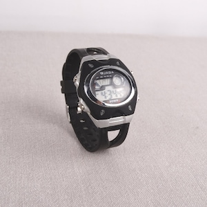 May include: Black and silver digital wristwatch with a black rubber band. The watch face has a digital display and a small analog clock.