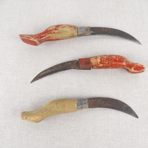 May include: Three vintage curved knives with wooden handles. The top knife has a red and white handle, the middle knife has a red handle, and the bottom knife has a natural wood handle.