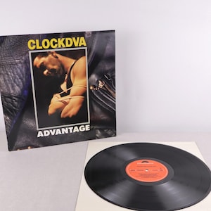 May include: A vinyl record album titled "Advantage" by Clock DVA. The album cover features a man in a leather jacket with the band's name in yellow. A black vinyl record is on a white sleeve.
