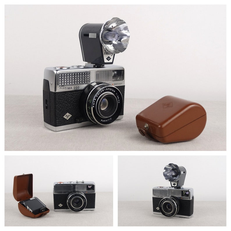 May include: A silver and black 35mm film camera with a built-in flash and a brown leather case. The camera has a lens labeled "Auta Color-Apotar 1:2.8" and "Paratic". The camera is labeled "Optima 200".