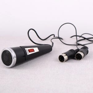 May include: Black vintage microphone with a silver rim and a red switch. The microphone has a black cable and two connectors. The brand name "Philips" is visible on the microphone.