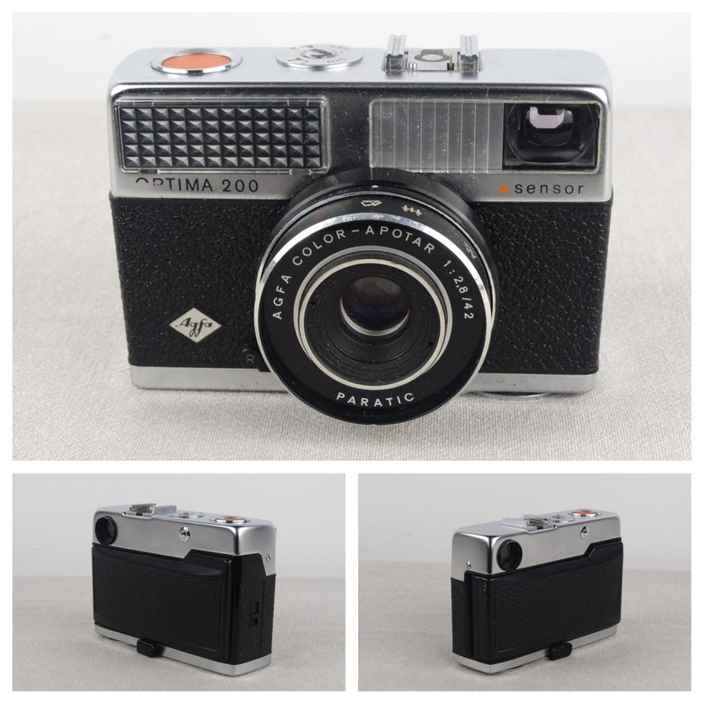 May include: A black and silver Agfa Optima 200 35mm film camera with a silver lens and a black leatherette body. The camera has a built-in flash and a viewfinder on the top. The lens is labeled "Agfa Color-Apotar 1:2.8/42 Paratic".