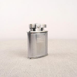 以下が含まれることがあります： テクスチャ加工が施されたデザインとフリップトップの蓋が付いたシルバーのライター