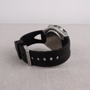 May include: A black and silver digital wristwatch with a black rubber band. The watch has a silver face and a black digital display.