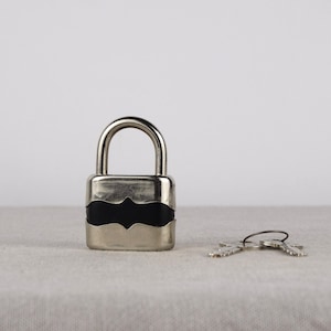 May include: A silver padlock with a black plastic insert and two silver keys.