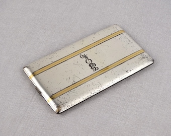 Puede incluir: Un estuche rectangular de plata y oro con una inicial "M" grabada en el centro. El estuche tiene dos rayas doradas que corren horizontalmente a través de la superficie.
