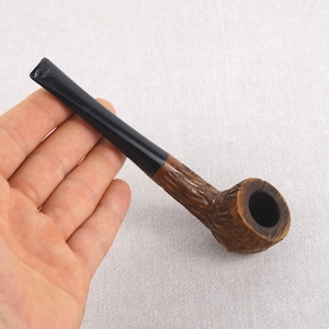 May include: A brown wooden pipe with a black mouthpiece. The pipe has a carved design and a bowl with a round opening.