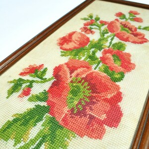 May include: A framed cross-stitch embroidery featuring a bouquet of red flowers with green leaves on a white background.