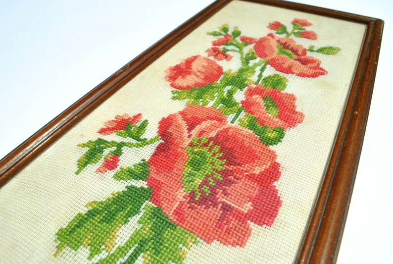 May include: A framed cross-stitch embroidery featuring a bouquet of red flowers with green leaves on a white background.